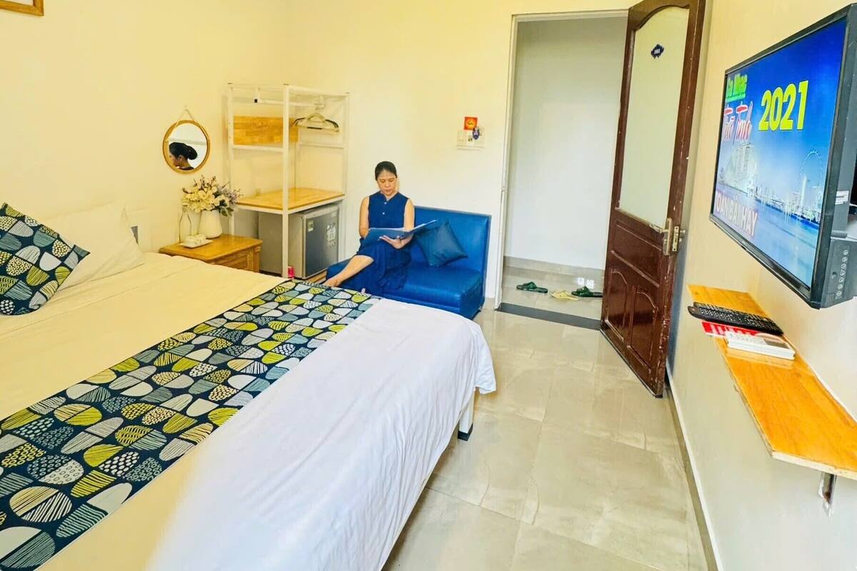 A hotel room with a bed, a desk, a chair, a television, and a door leading to another room.