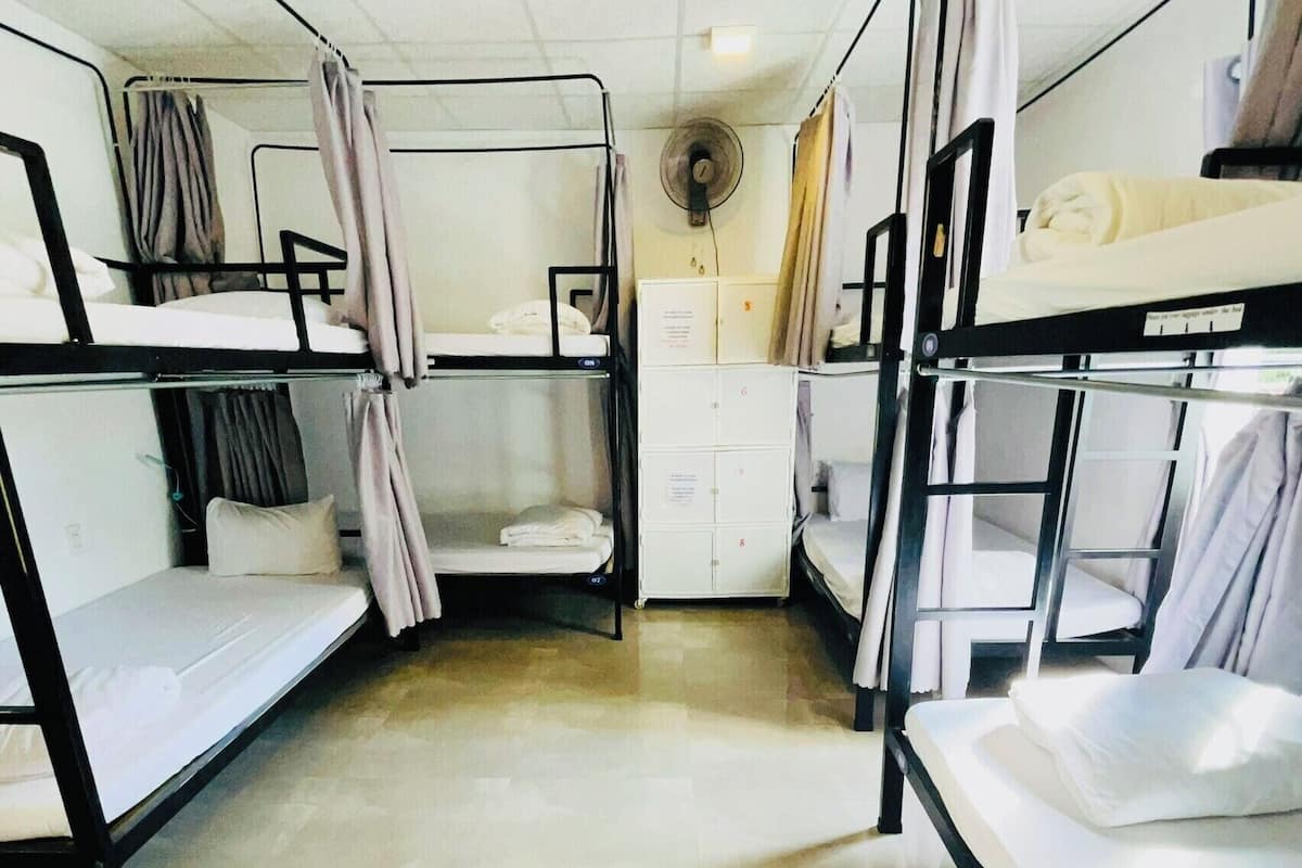 A dormitory room with bunk beds, a fan, and a small cabinet.