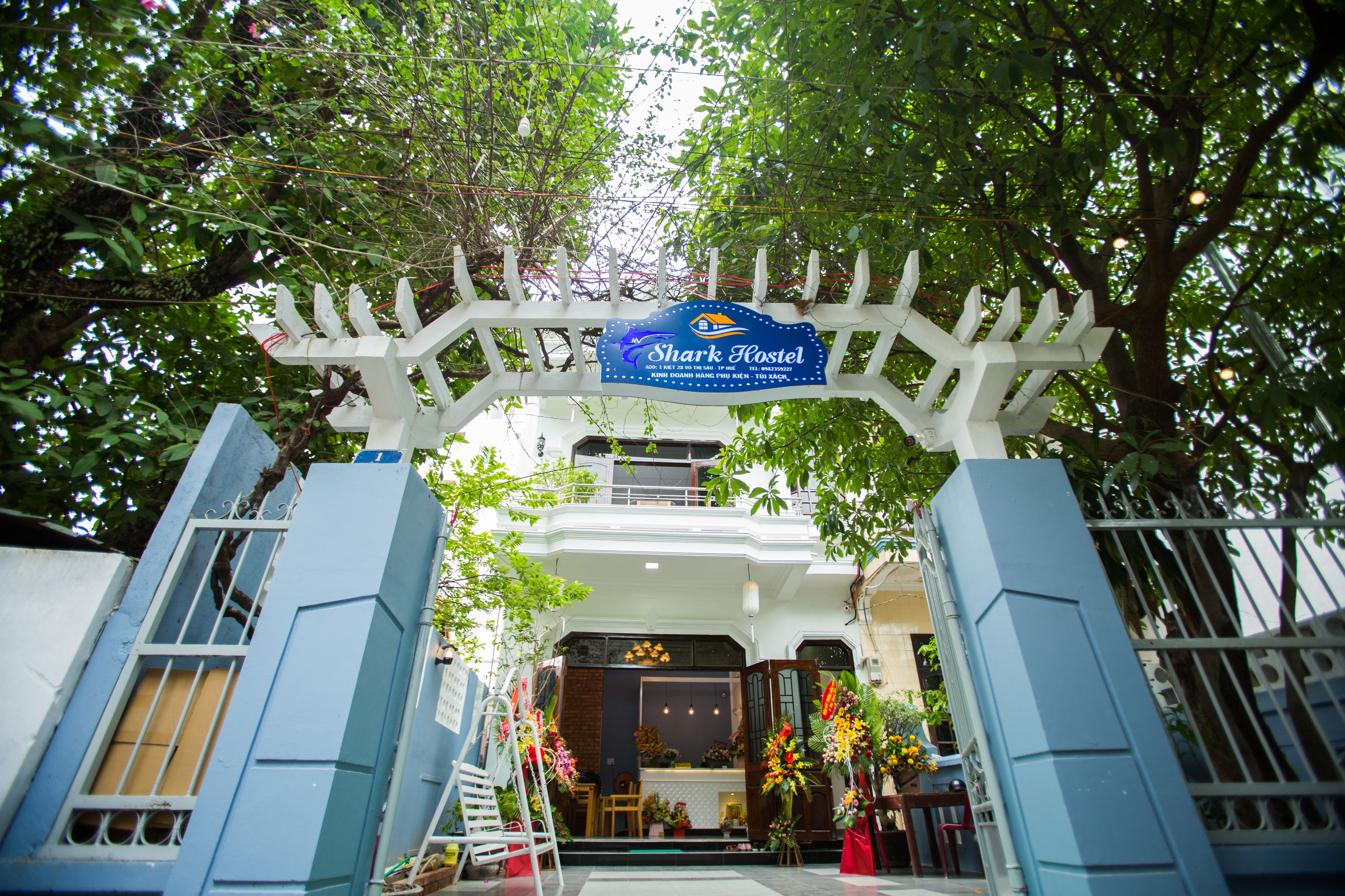 A white gate with a blue sign reading "Shark Hostel" and a white fence.