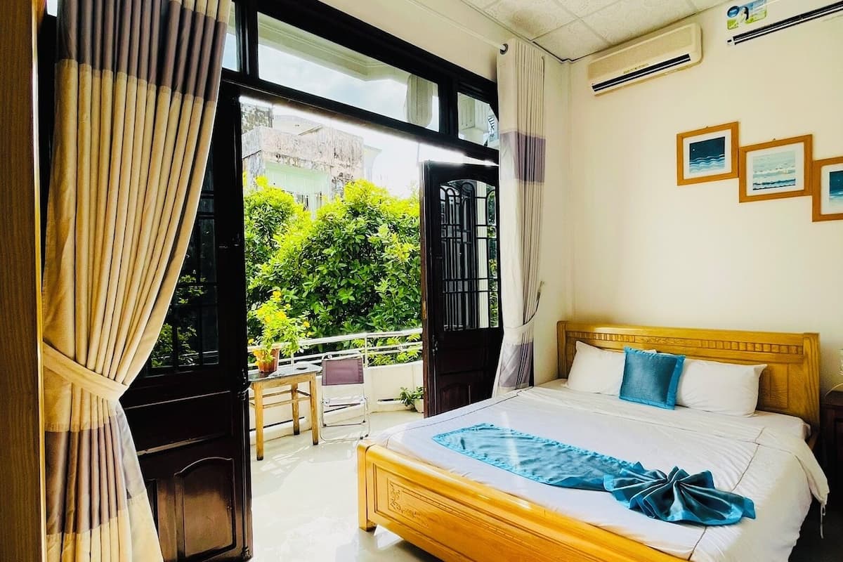 A bedroom with a wooden bed, a view of greenery outside, and a ceiling with a patterned design.
