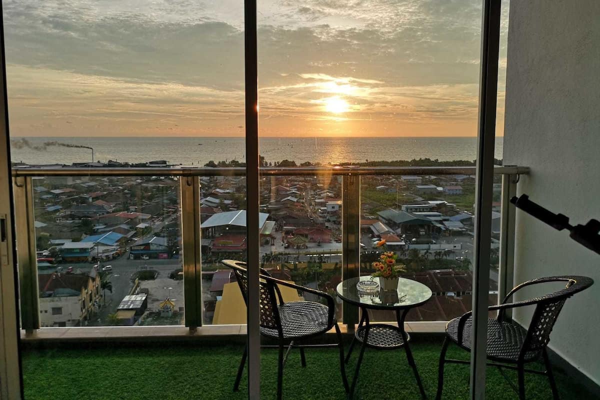 A balcony with a glass railing, two wicker chairs, a small round table, and a vase of flowers.