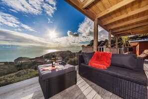 Un balcón con sofá y mesa de mimbre, con vistas a un paisaje costero y una pérgola de madera.