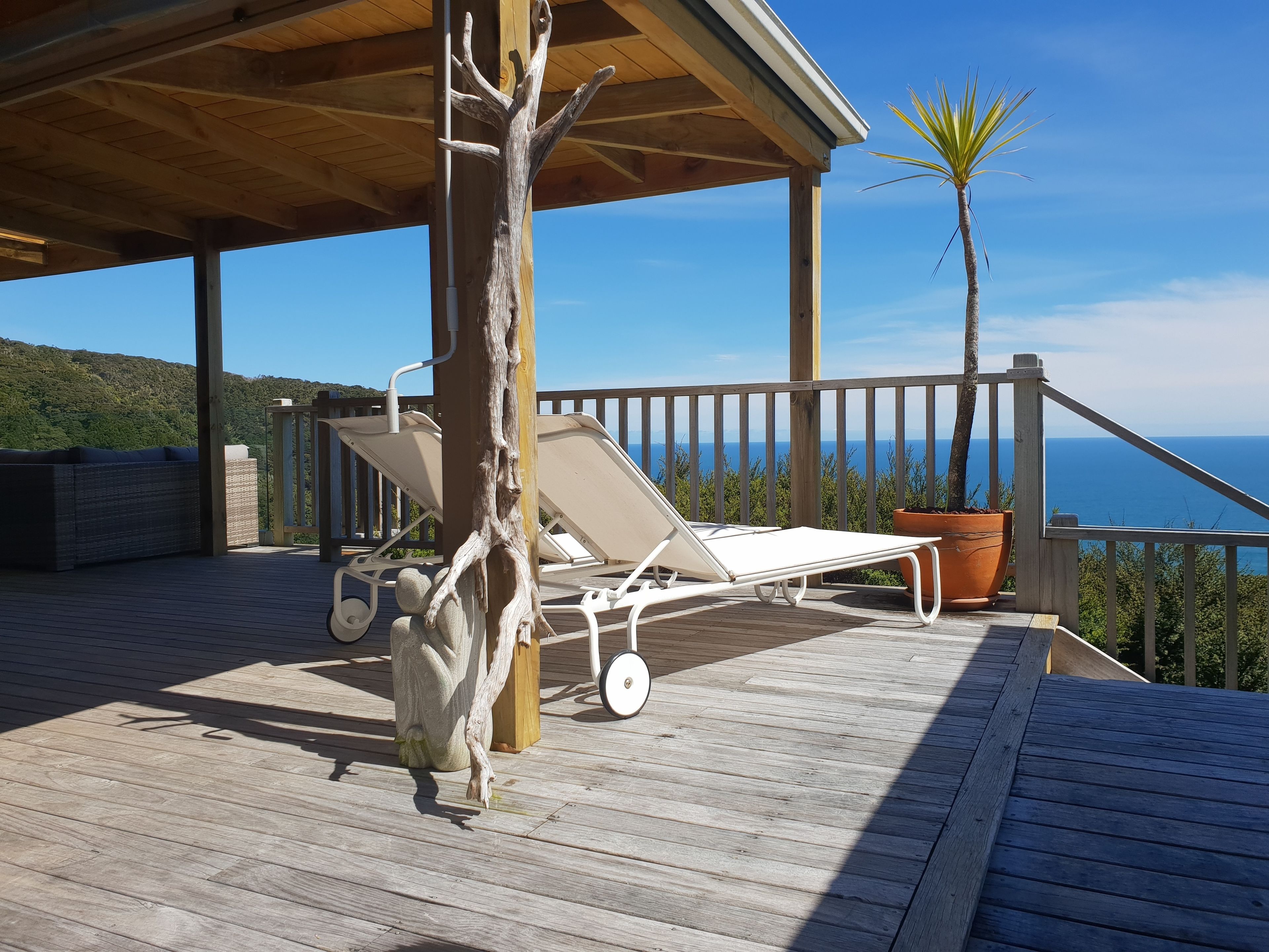 A wooden deck with a lounge chair and a potted plant, overlooking a scenic view.