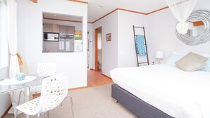Une chambre avec un grand lit, un bureau avec une chaise, une petite table et une vue sur la cuisine.
