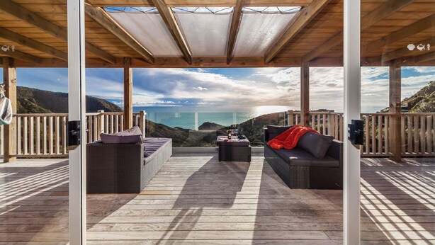 Un espace extérieur abrité, doté de sièges et offrant une vue sur la mer, avec des meubles en osier et une terrasse en bois.