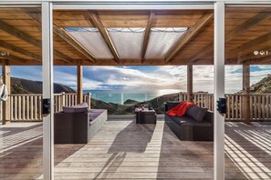 A covered outdoor seating area with a view of the sea, featuring wicker furniture and a wooden deck.