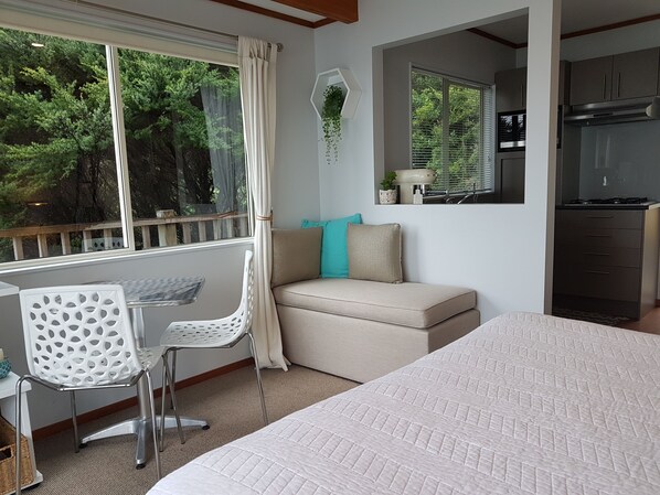 A bedroom with a large bed, a window with curtains, a sofa with cushions, a chair, and a small table.
