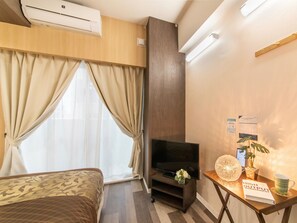 Habitación de hotel con cama, televisión, escritorio con un libro y una planta.