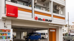 A Mr. Kinjo hotel with a parking garage entrance, vending machines, and a blue car parked inside. - Mr.KINJO in UCHIDOMARI (Ginowan)