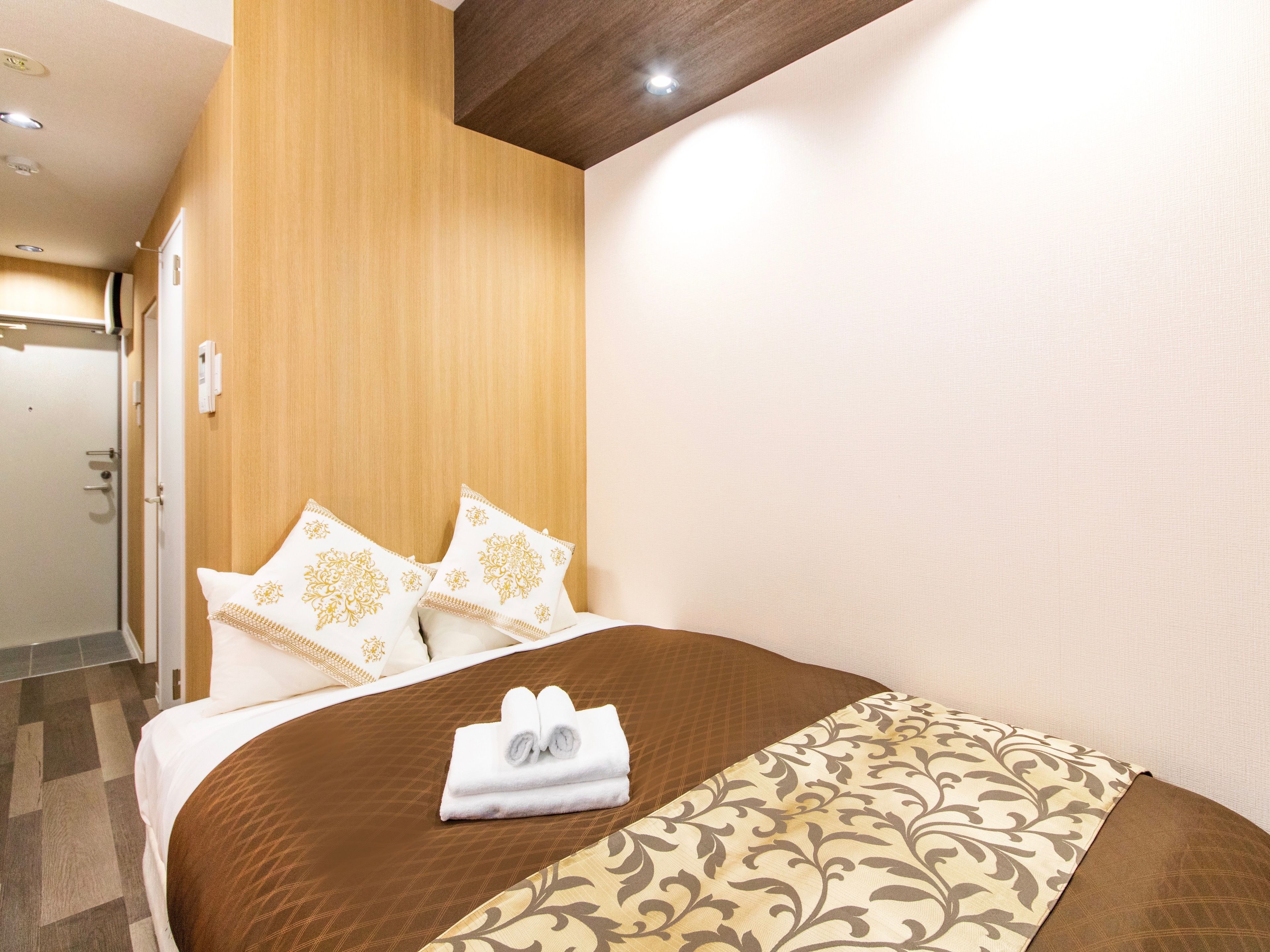 Quarto de hotel com uma cama, cabeceira de madeira e colcha marrom e bege com padrão.