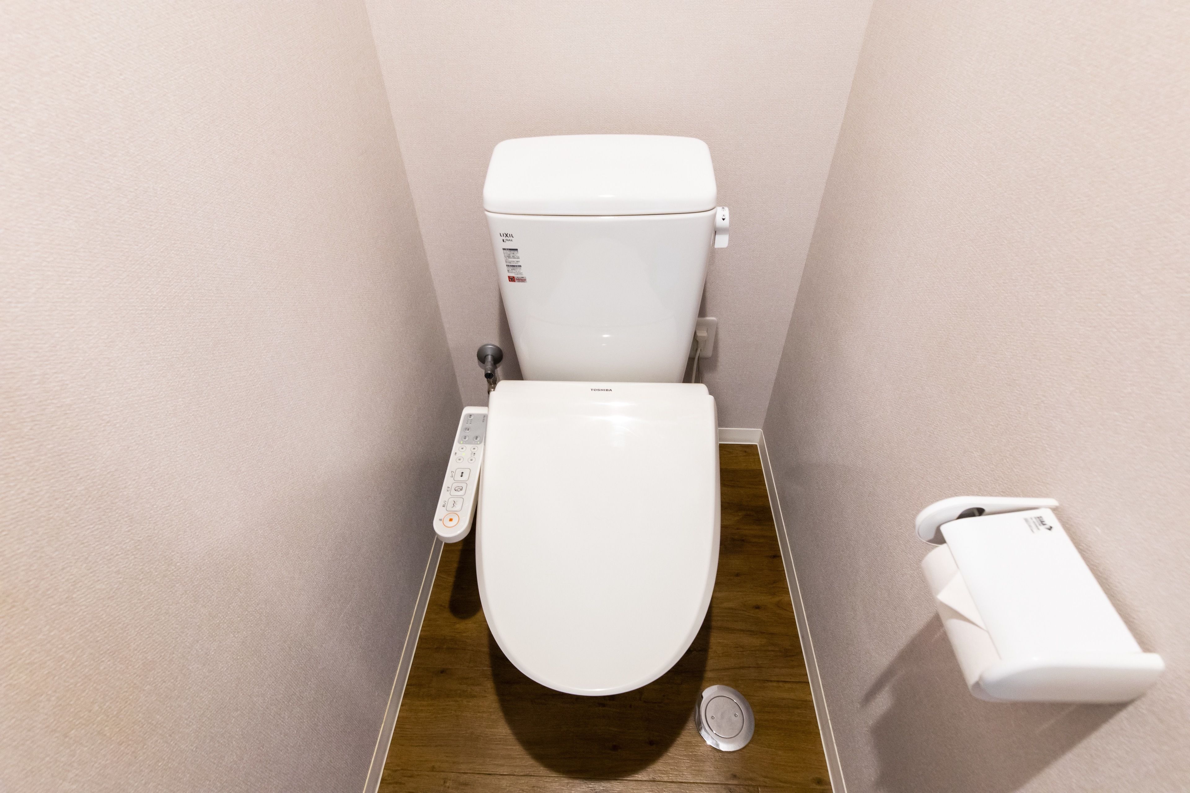A small, modern bathroom with a white toilet, a control panel, and a toilet paper holder.