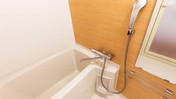 A white bathtub with a shower head and hose, a wooden panel wall, and a small window with a view.
