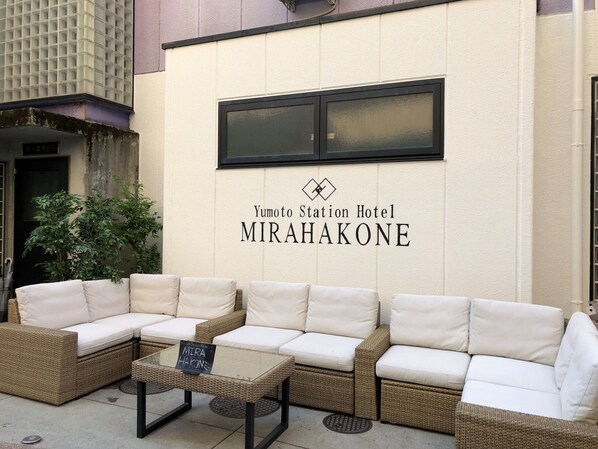 A corner seating area with wicker furniture and a sign for Yumoto Station Hotel MIRAHAKONE. - Yumoto Station Hotel MIRAHAKONE (Hakone)