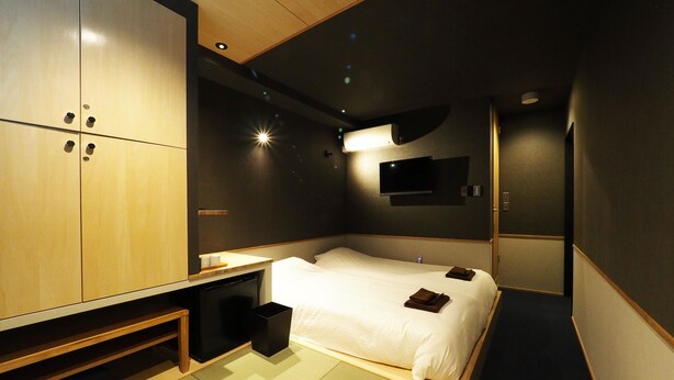 Una habitación de hotel moderna con cama, mesita de noche, armario y televisión de pantalla plana montada en la pared.