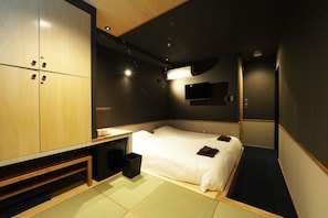 Une chambre d’hôtel moderne équipée d’un lit, d’une table de chevet, d’une armoire et d’un téléviseur à écran plat fixé au mur.