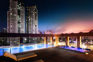 A rooftop pool with a city skyline view, a hot tub, and lounge chairs.