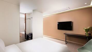 A modern hotel room with a large bed, a flat-screen TV mounted on the wall, a small desk, and a green chair.