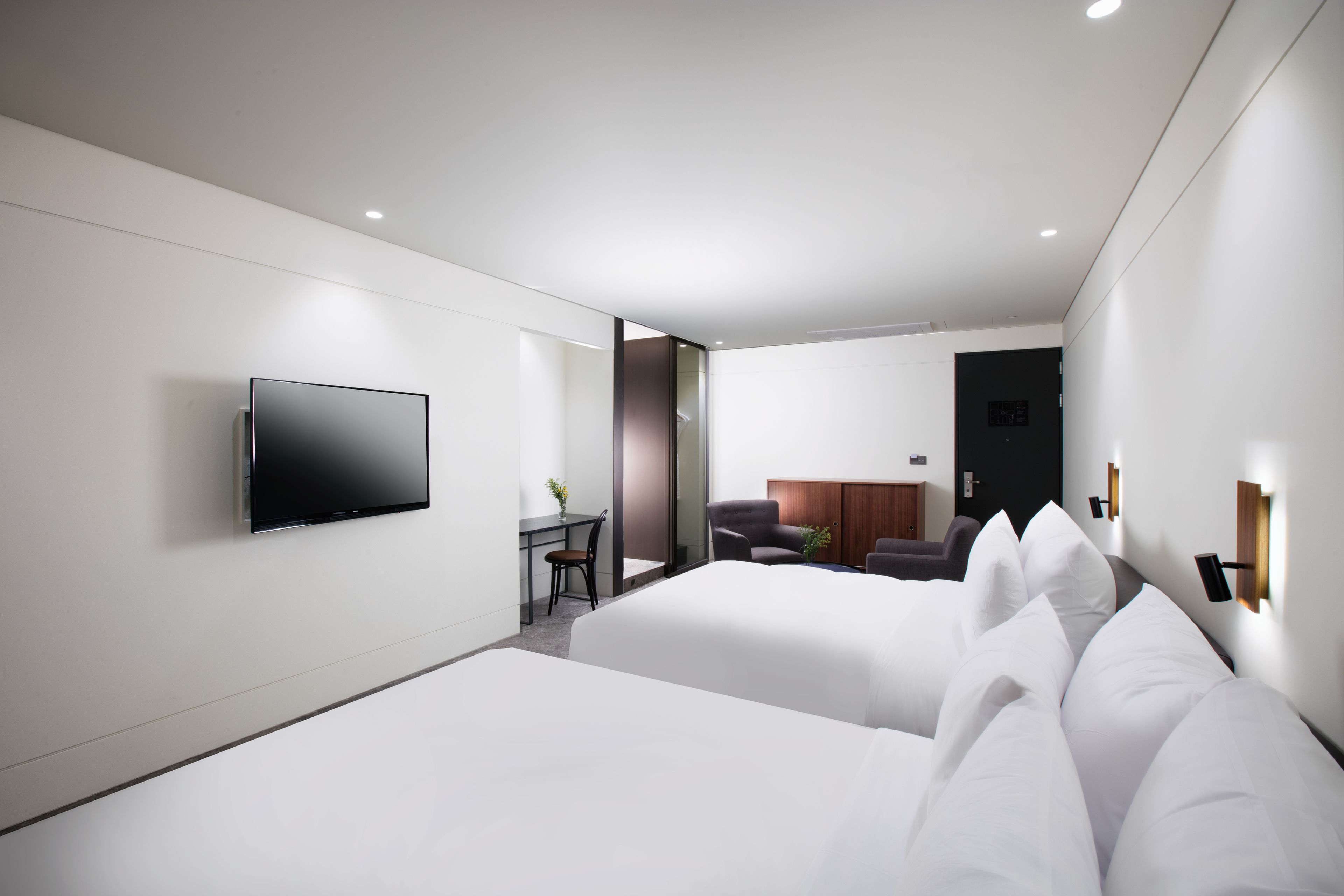 Een moderne hotelkamer met twee bedden, een flatscreen televisie, een bureau met stoel en een zithoek met een bank en een plant.