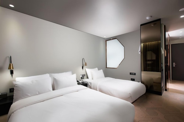 Una habitación de hotel moderna con dos camas, un espejo grande y una puerta de vidrio que da a un baño.
