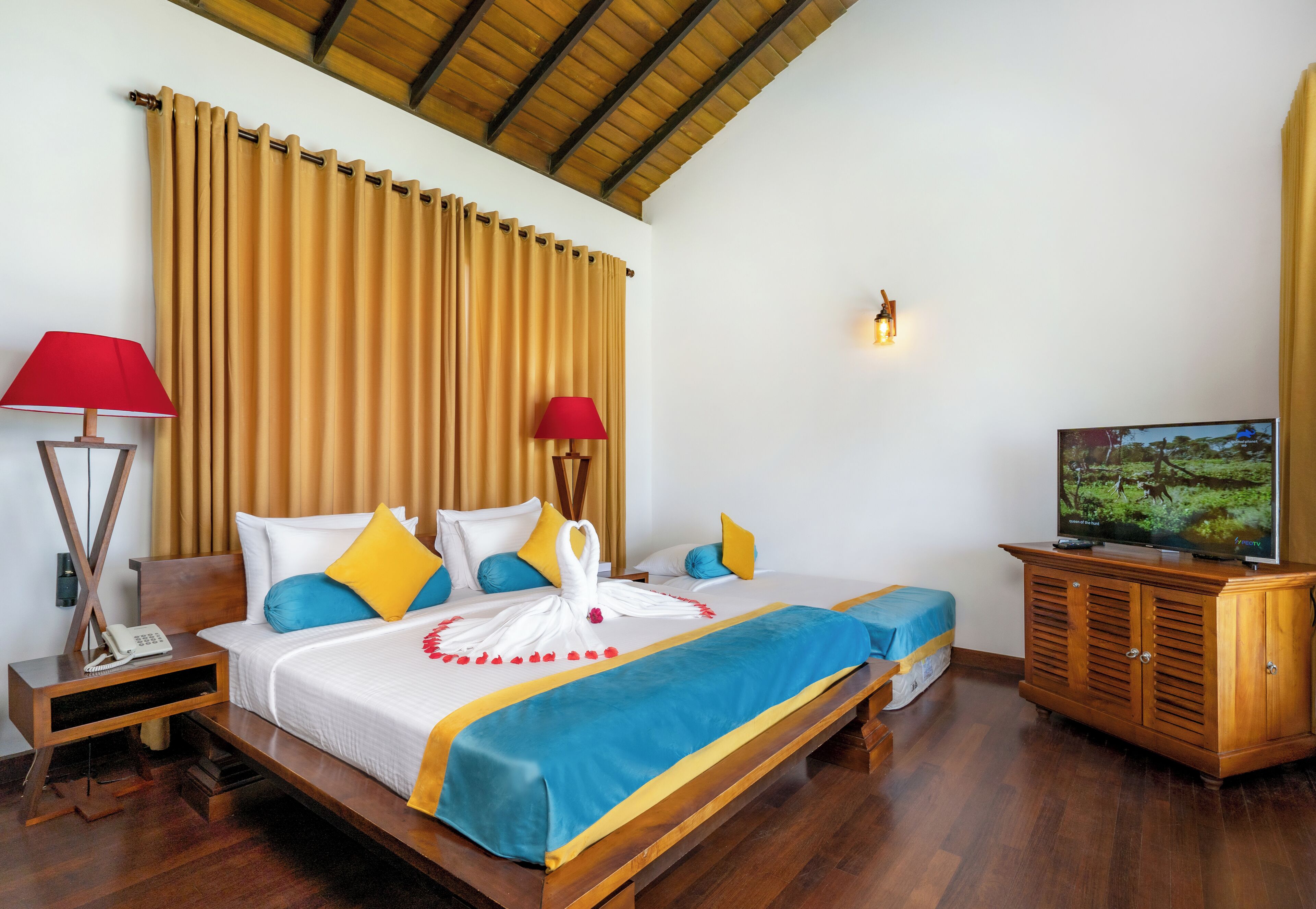 Habitación de hotel con cama, televisor, aparador de madera y mesita de noche con lámpara y teléfono.