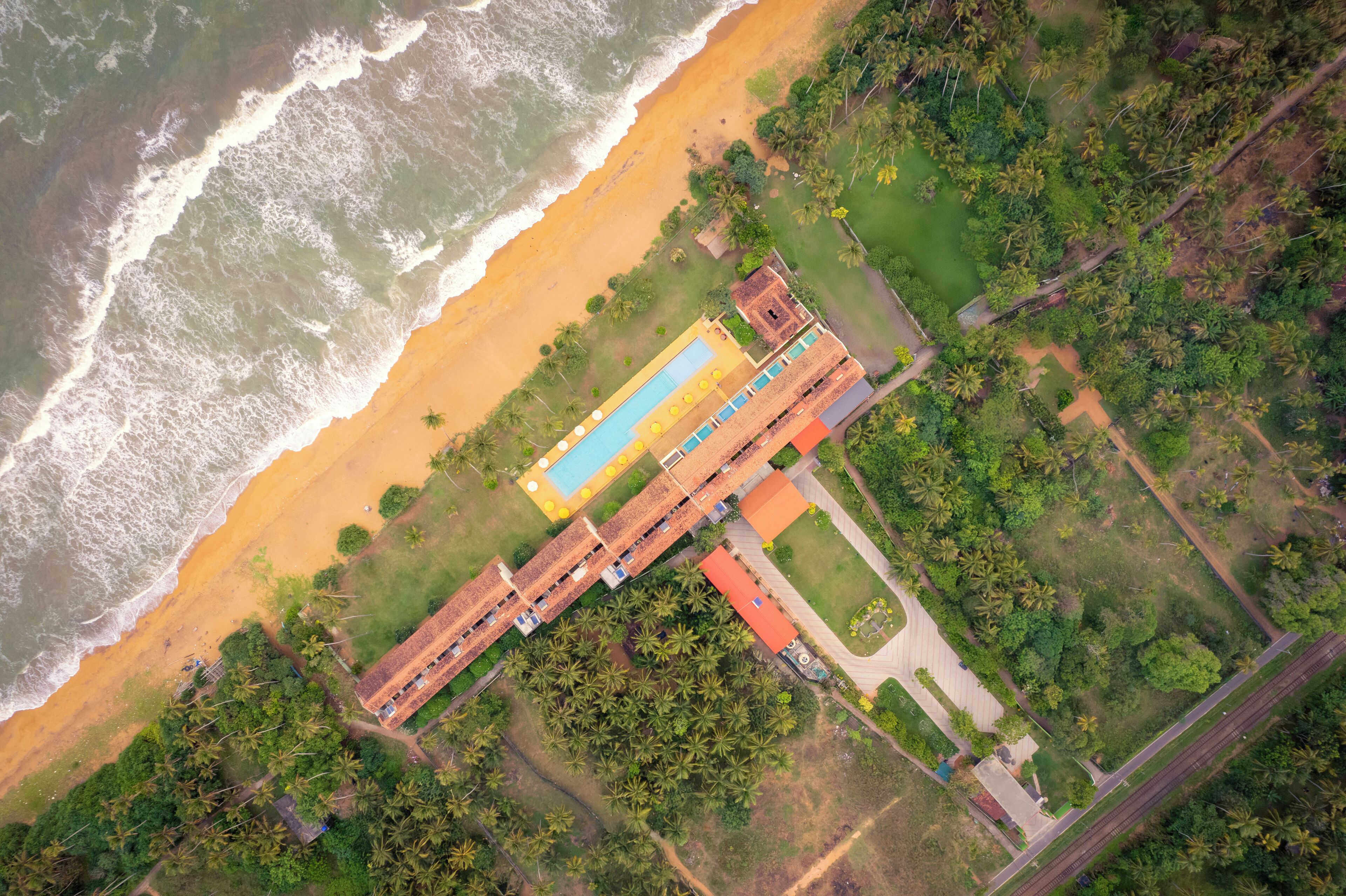 Vista aérea de um resort com piscina, acesso à praia e vegetação exuberante.