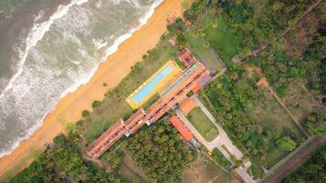 Vista aérea de um resort com piscina, acesso à praia e vegetação exuberante.