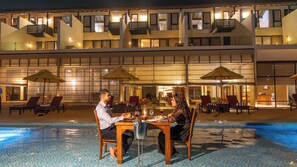 A poolside dining area with tables and chairs, a pool, and a building with multiple balconies and windows. - Grand Beach Hotel Wadduwa (Wadduwa)