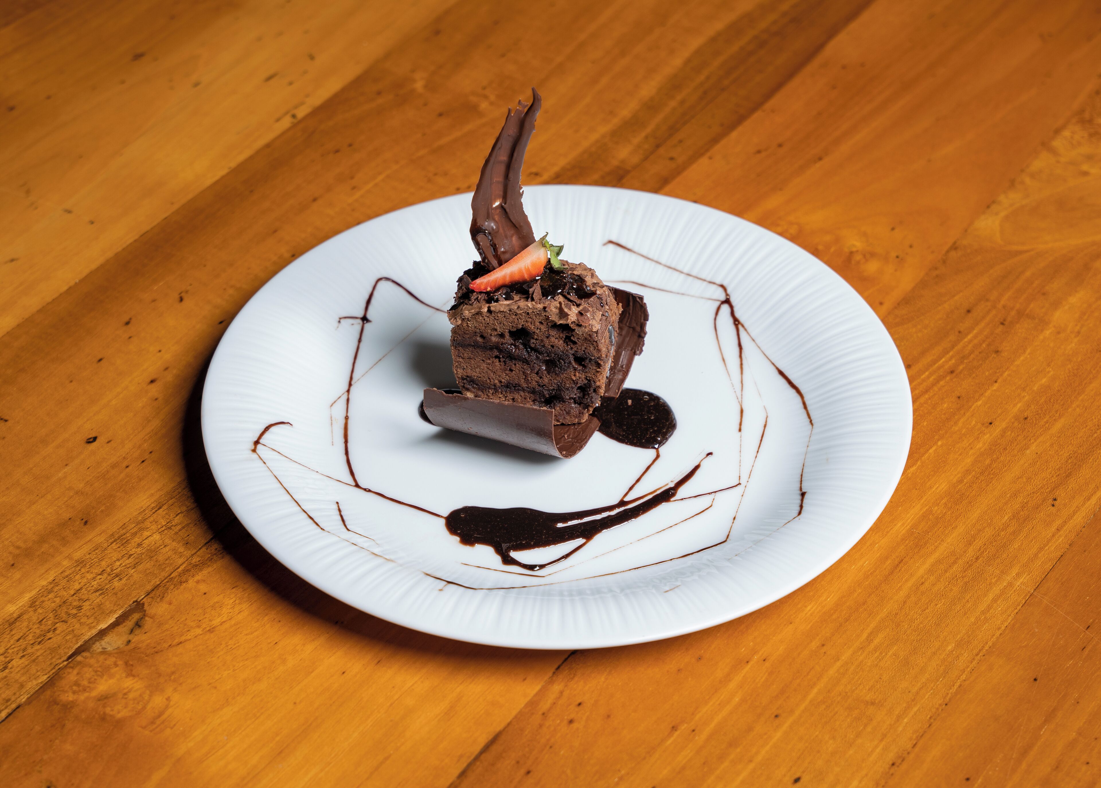 A dessert on a white plate with chocolate and a carrot on top, placed on a wooden table.