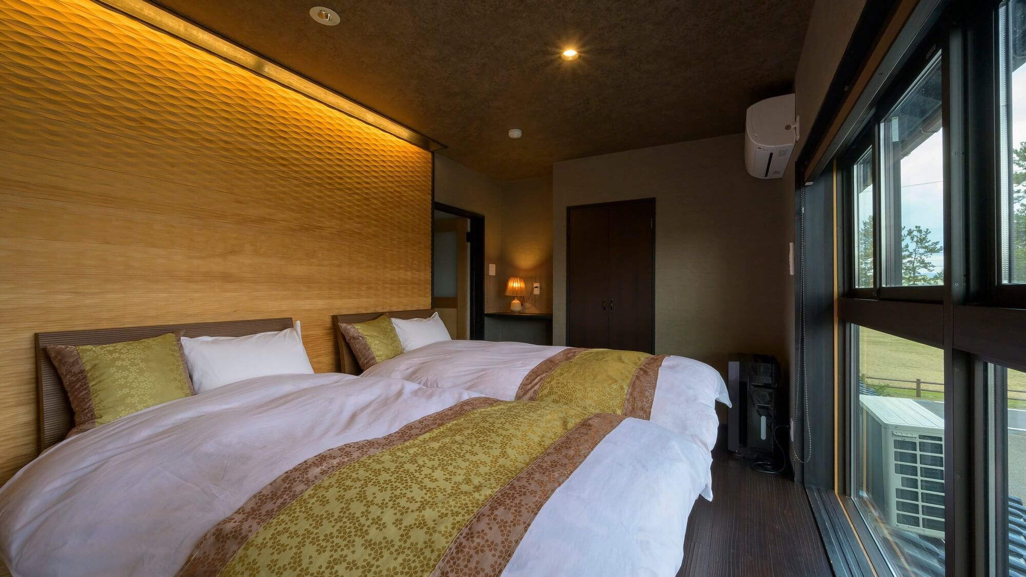 Une chambre d’hôtel avec un grand lit, une tête de lit en bois, une fenêtre donnant sur un beau paysage et un climatiseur fixé au mur.