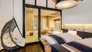 A modern bedroom with a hanging chair, a bed with a striped bedspread, and a view of a traditional Japanese room. - Asahiya (Himi)