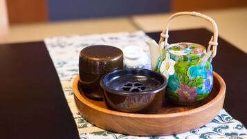 A wooden tray with a decorative teapot, a small bowl, and a bottle on a patterned tablecloth.