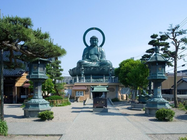 A large Buddha statue in a courtyard with traditional Japanese architecture in the background.