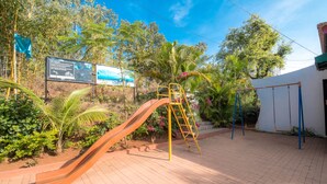 A playground with a slide, a swing set, and informational signs. - Umbrella Inn (Mahabaleshwar)