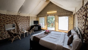 A tent-style room with a bed, a desk, a chair, and a television. - Umbrella Inn (Mahabaleshwar)