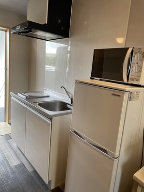 A compact kitchen with a stainless steel sink, a built-in microwave, and a refrigerator. - HYGGE Biimata (Nago)