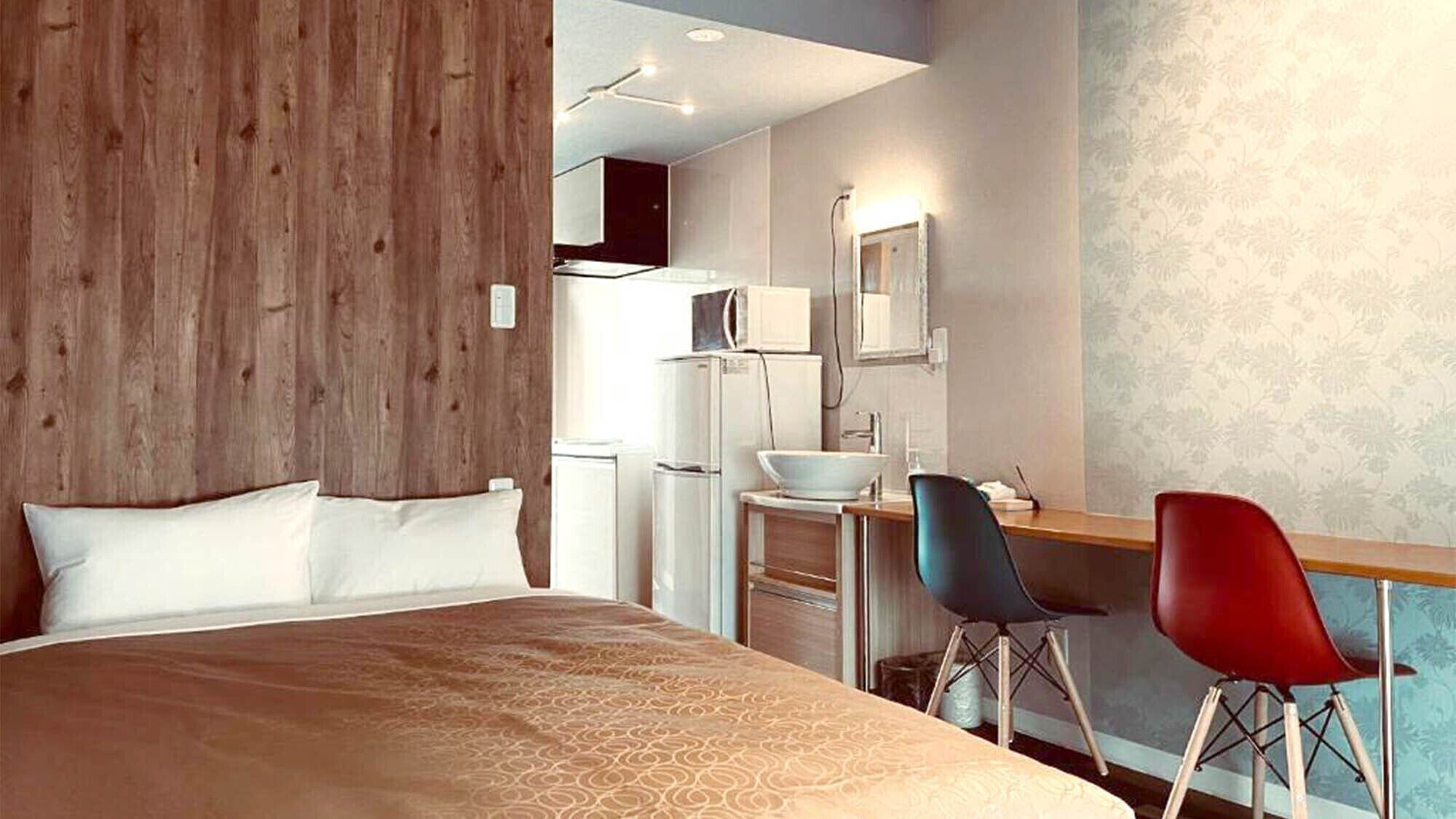 A hotel room with a bed, a desk with two chairs, a microwave, and a refrigerator.