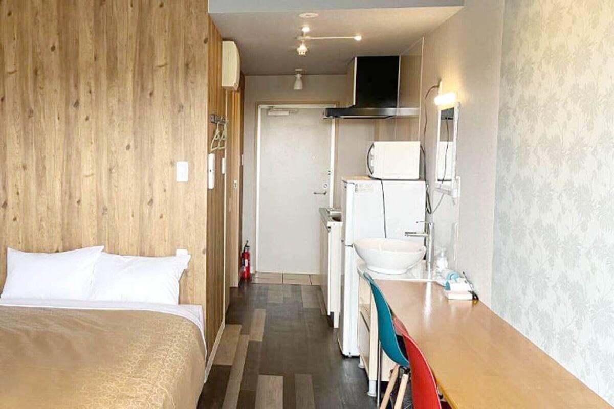 A hotel room with a bed, a wooden wall, a kitchenette, and a bathroom.