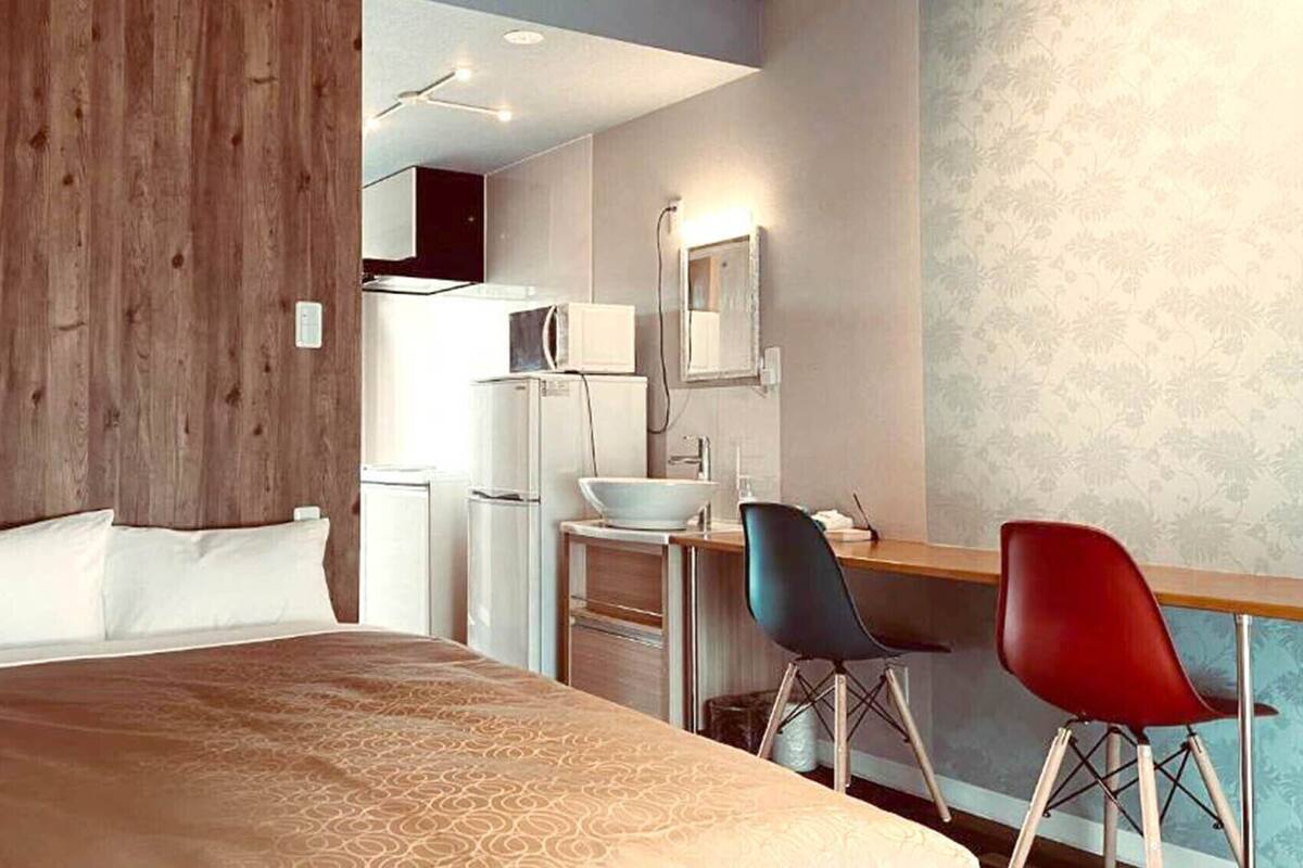A hotel room with a bed, a desk with two chairs, a microwave, and a sink.