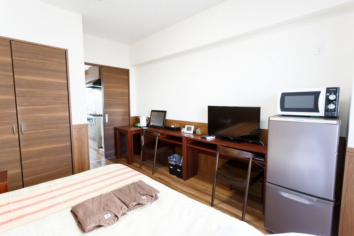 Habitació d'hotel senzilla amb llit, escriptori amb ordinador, televisió i nevera.