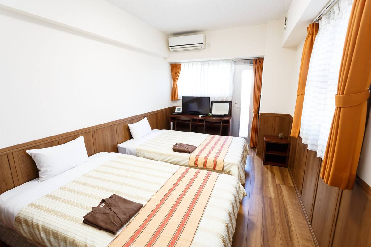 Una habitació d'hotel amb dos llits, una televisió, un escriptori i un aparell d'aire condicionat.