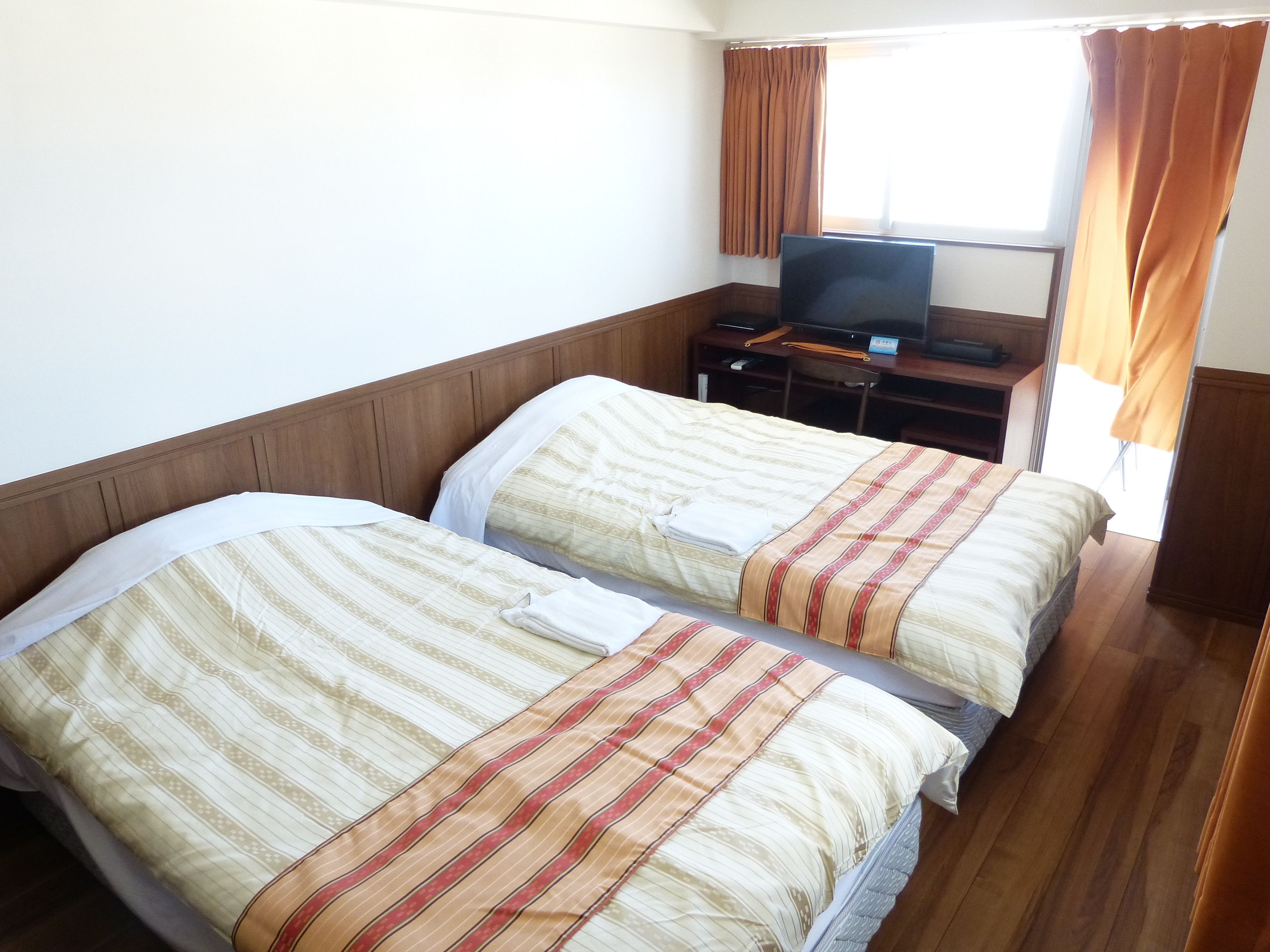 Una habitación de hotel con dos camas, un televisor sobre un mueble de madera y una ventana con cortinas.
