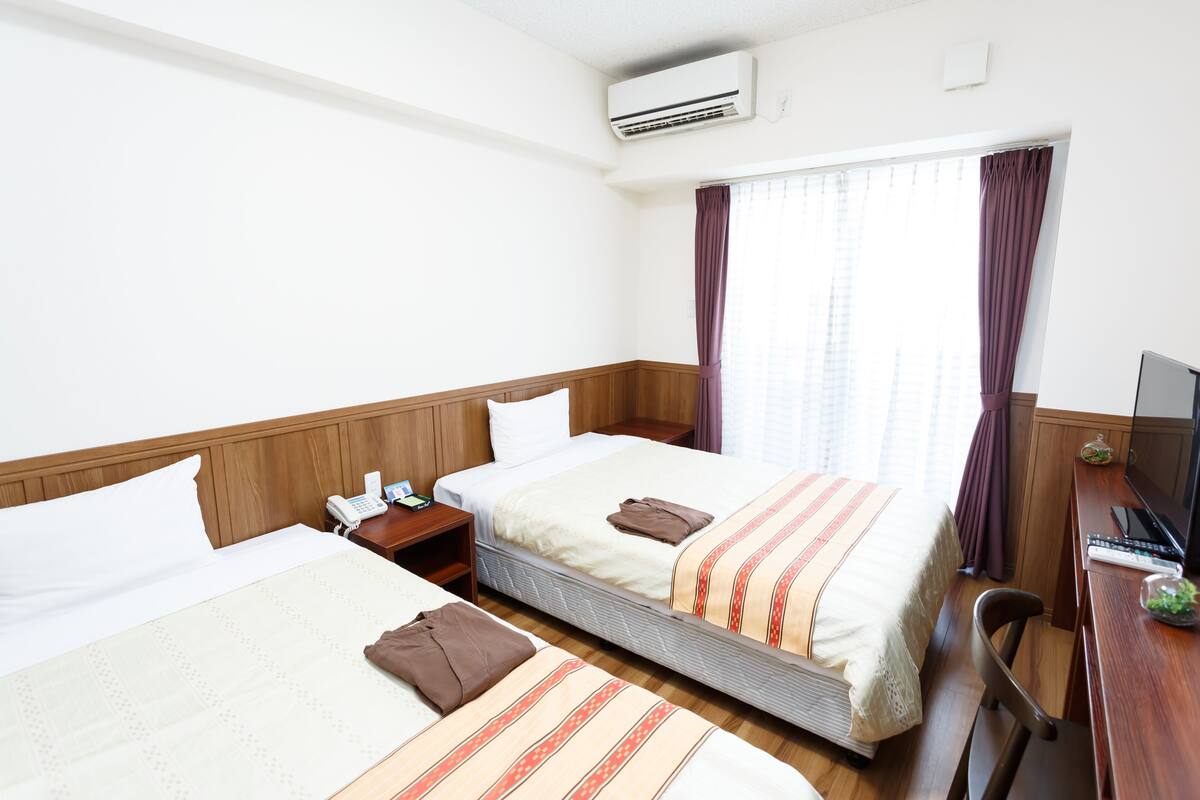 Habitació d'hotel amb dos llits, un escriptori amb un ordinador i un aparell d'aire condicionat.