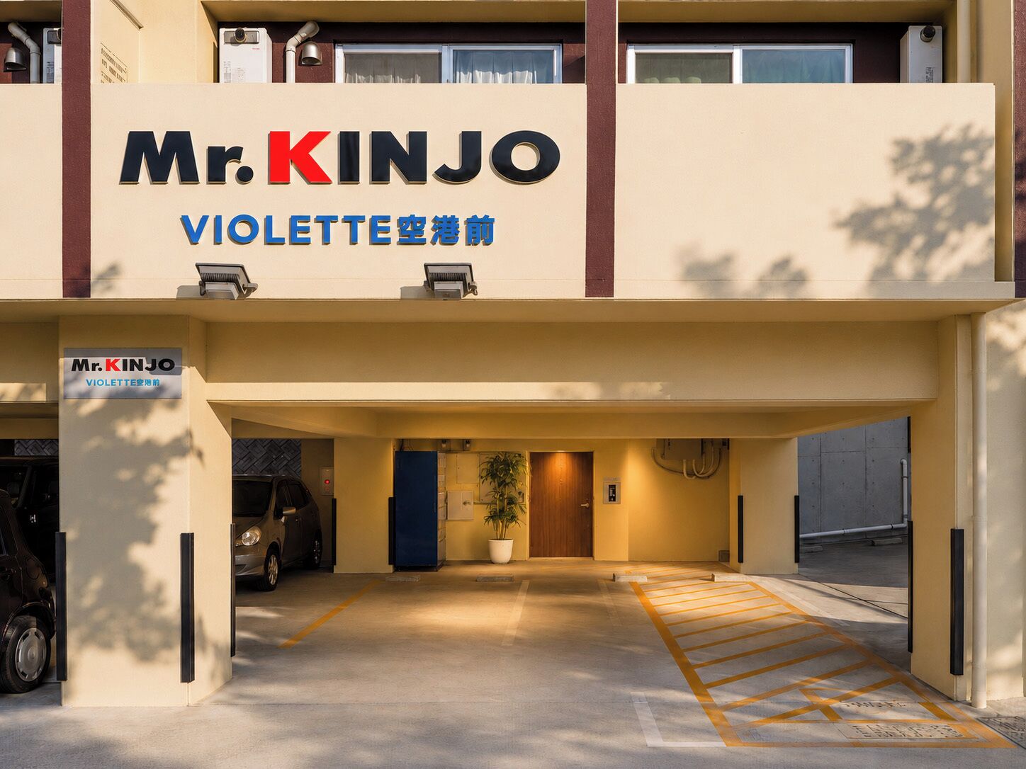 A hotel entrance with a sign reading 'Mr. KINJO VIOLETTE' and a parking area with marked spaces.