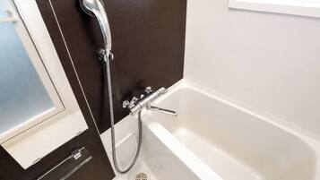 A bathroom with a bathtub, a showerhead, and a window.