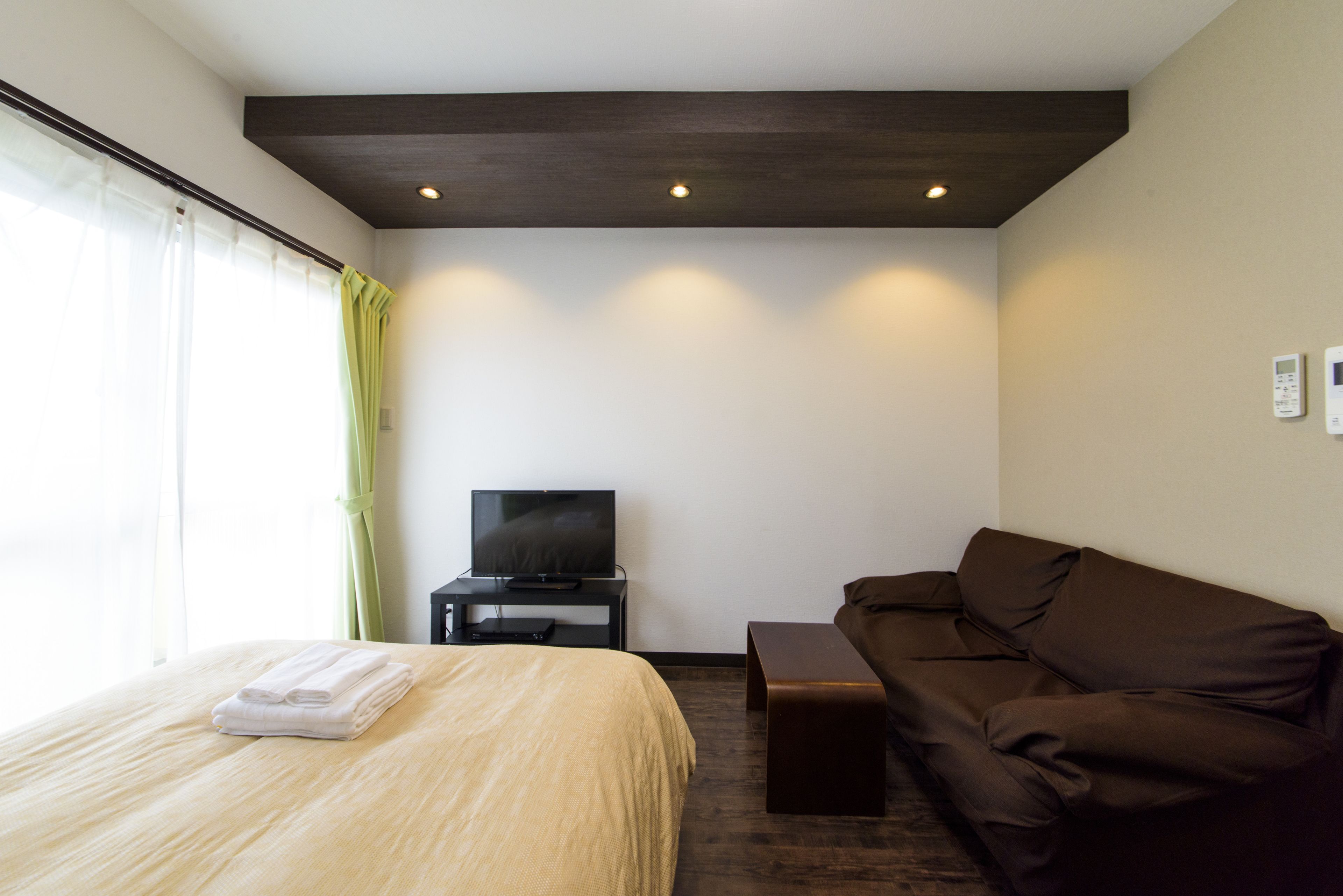 A hotel room with a bed, a television on a stand, a brown sofa, and a window with curtains.