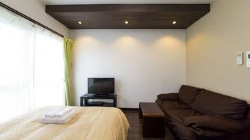 A hotel room with a bed, a television on a stand, a brown sofa, and a window with curtains.