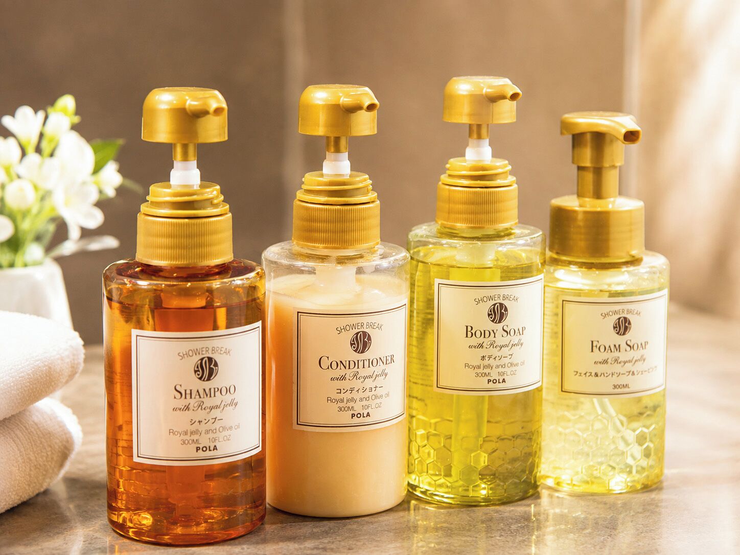 Cuatro botellas de productos de baño con dosificadores, incluyendo champú, acondicionador, jabón corporal y jabón espuma, dispuestas sobre una superficie.