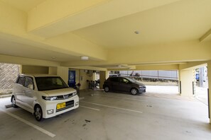 A parking garage with two cars parked, a bicycle, and a blue sign. - Mr.KINJO VIOLETTE KUKOMAE (Naha)