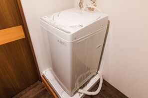 Een compacte, witte, inbouw wasmachine in een hoek, met een houten deurkozijn.