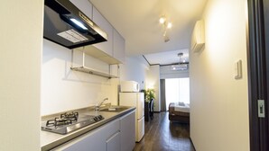 A compact kitchen with a gas stove, sink, and white cabinets. A small refrigerator is visible in the background. - Mr.KINJO in MATSUYAMA (Naha)